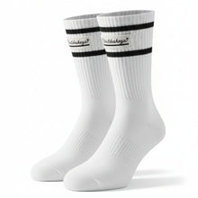 A pair of white crew socks with black stripes and a 'Chubbies' logo on the cuffs, laid flat on a black textured surface.