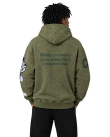Back view of male model wearing an oversized olive green washed hoodie with graphic sleeve patches and self worth text design, styled with black pants in a clean white studio setting.